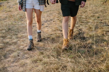 Téléchargez les photos : Un homme et une fille marchent ensemble en se tenant la main lors d'une randonnée dans les montagnes. Jambes en gros plan. - en image libre de droit