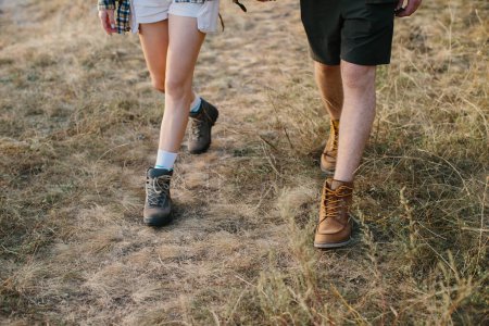 Foto de Un chico y una chica caminan juntos tomados de la mano durante una caminata por las montañas. Primer plano de las piernas. - Imagen libre de derechos