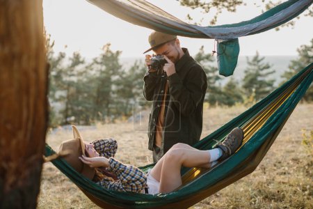 Photo for Couple having fun relaxing in hammocks outdoors. A guy takes a picture of a girl on a film camera. - Royalty Free Image