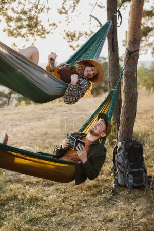 Téléchargez les photos : Un mec et une fille se détendent dans des hamacs dans une forêt de pins au coucher du soleil. - en image libre de droit