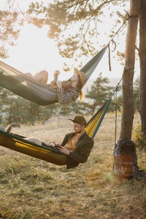 Photo for A guy and a girl are relaxing in hammocks in a pine forest at sunset. - Royalty Free Image