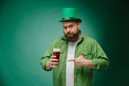 Foto de Hombre emocional barbudo con cerveza sobre un fondo verde oscuro. Banner del Día de San Patricio - Imagen libre de derechos