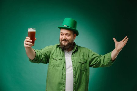Téléchargez les photos : Heureux homme barbu avec un verre de bière sur un fond vert foncé. Célébration de la Saint Patrick - en image libre de droit