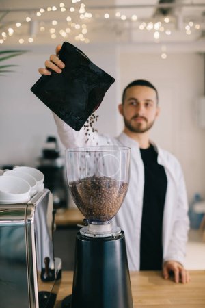 Téléchargez les photos : Un barista masculin verse des grains de café dans un moulin à café. - en image libre de droit