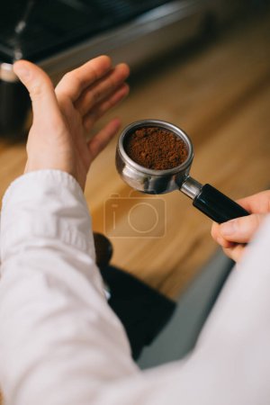 Foto de La mano del camarero sostiene un soporte con café fresco molido para hacer café en una máquina de café. Primer plano - Imagen libre de derechos