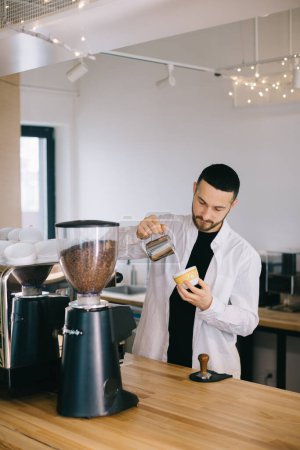 Téléchargez les photos : Un barista près d'une machine à expresso prépare un délicieux café. Un jeune homme prépare un café dans un café. - en image libre de droit