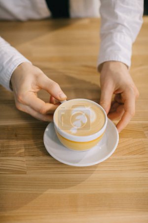 Téléchargez les photos : Les mains du barista tiennent un délicieux cappuccino. Gros plan, vue de dessus. - en image libre de droit