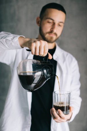 Foto de Barista guapo verter café recién hecho goteo en una taza de vidrio. Preparación de café método alternativo. - Imagen libre de derechos