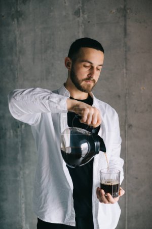 Photo for Handsome barista pouring freshly brewed drip coffee in a glass mug. Preparing coffee alternative method. - Royalty Free Image