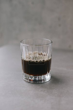 Téléchargez les photos : Café goutte à goutte fraîchement brassé dans une tasse en verre. Une tasse de café sur fond gris. - en image libre de droit