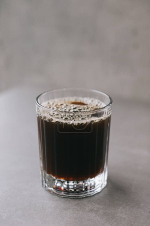 Foto de Café recién hecho goteo en una taza de vidrio. Una taza de café sobre un fondo gris. - Imagen libre de derechos