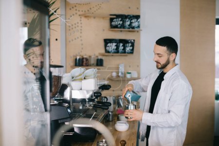 Téléchargez les photos : Un barista près d'une machine à expresso prépare un délicieux café. Un jeune homme prépare un café dans un café. - en image libre de droit
