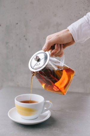 Foto de La mano de un camarero vierte té aromático en una taza, aislada sobre un fondo gris. - Imagen libre de derechos
