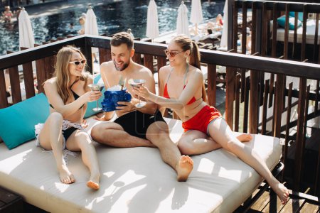 Téléchargez les photos : Un groupe d'amis joyeux se détend avec des cocktails au bord de la piscine. - en image libre de droit
