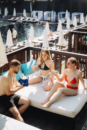 Téléchargez les photos : Un groupe d'amis joyeux se détend avec des cocktails au bord de la piscine. - en image libre de droit