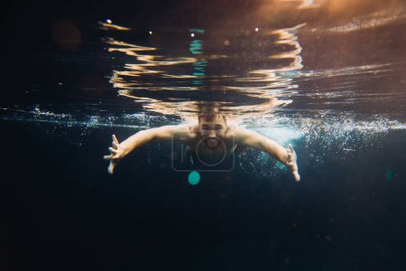 Foto de Un joven nada en una piscina, bajo el agua. Concepto de vacaciones y vida despreocupada. - Imagen libre de derechos