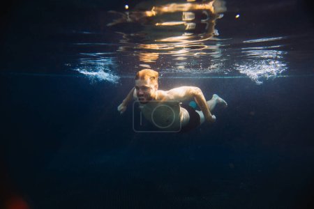 Téléchargez les photos : Un jeune homme nage sous l'eau dans une piscine. Concept vacances d'été. - en image libre de droit