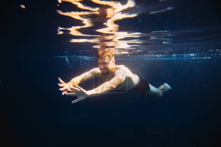 Téléchargez les photos : Un beau jeune homme nage sous l'eau dans une piscine pendant ses vacances. - en image libre de droit