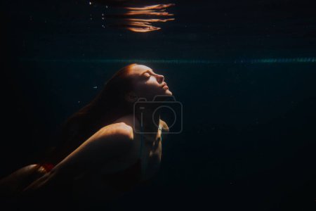 Photo for Young redheaded woman swimming underwater in a poo - Royalty Free Image