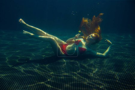 Photo for A beautiful red-haired woman poses with a cocktail under water. - Royalty Free Image