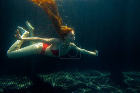 Téléchargez les photos : Une belle fille sportive pose sous l'eau avec des cheveux lâches contre les rayons lumineux du soleil de la surface. - en image libre de droit