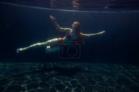 Photo for A beautiful sporty girl poses underwater with loose hair against the bright rays of the sun from the surface. - Royalty Free Image