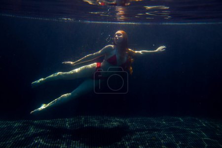 Foto de Una hermosa chica deportiva posa bajo el agua con el pelo suelto contra los brillantes rayos del sol de la superficie. - Imagen libre de derechos