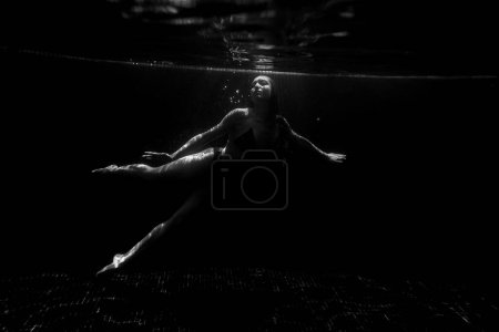 Téléchargez les photos : Une belle fille sportive pose sous l'eau avec des cheveux lâches contre les rayons lumineux du soleil de la surface. BW - en image libre de droit