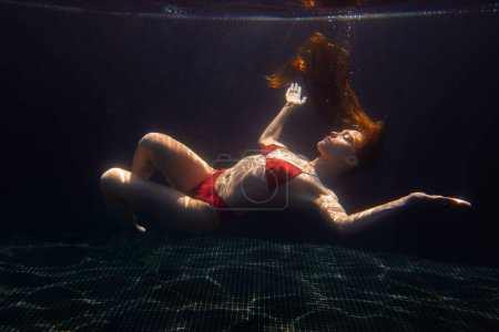 Foto de Una hermosa chica deportiva posa bajo el agua con el pelo suelto contra los brillantes rayos del sol de la superficie. - Imagen libre de derechos