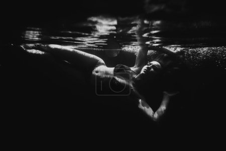 Foto de Una hermosa chica deportiva posa bajo el agua con el pelo suelto contra los brillantes rayos del sol de la superficie. BW - Imagen libre de derechos