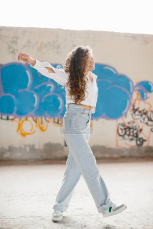 Photo for A stylish modern girl poses on the street against the background of graffiti. - Royalty Free Image