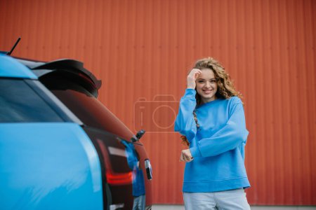 Foto de Una joven con estilo posa junto a su coche eléctrico. - Imagen libre de derechos