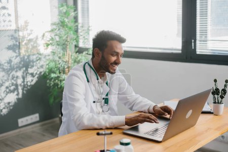 Photo for An Asian doctor uses a laptop to conduct an online consultation with a patient. - Royalty Free Image