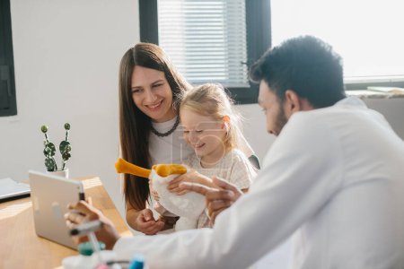 Photo for Cheerful mother and daughter visiting pediatrician at clinic, holding digital tablet and smiling, family having conversation with doctor. Modern technologies and healthcar - Royalty Free Image