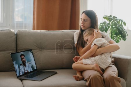 Foto de Consulta con un pediatra en línea. Una madre joven con un niño enfermo hace una videollamada a su médico. - Imagen libre de derechos