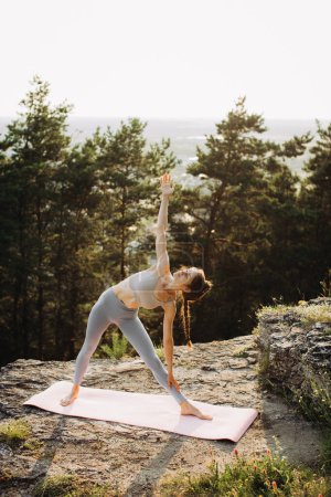 Photo for Flexible athletic young woman practices yoga on a rock in the mountains. - Royalty Free Image