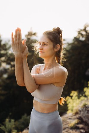 Téléchargez les photos : Fit jeune femme pratique le yoga sur les rochers sur le fond de la forêt de pins. Une belle fille médite et fait des exercices de respiration dans les montagnes. - en image libre de droit