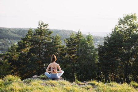 Foto de Vista trasera hermosa joven practicando yoga sobre roca en bosque de verano al aire libre. - Imagen libre de derechos