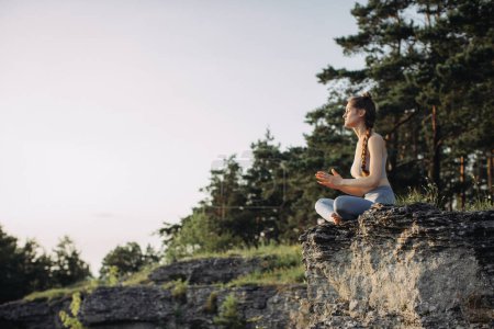 Téléchargez les photos : Une jeune femme pratique le yoga et médite dans les montagnes au coucher du soleil. Paix et unité avec la nature. - en image libre de droit