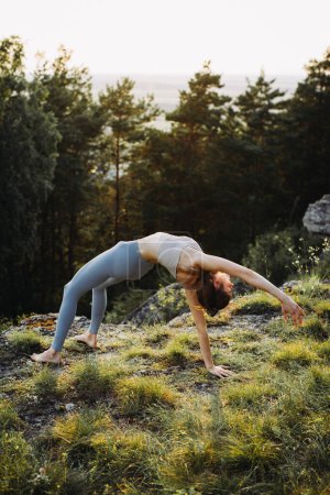 Téléchargez les photos : Une jeune femme pratique le yoga dans les montagnes sur fond de pinède. - en image libre de droit