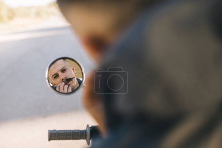 Biker man is reflected in the mirror of his motorcycle.