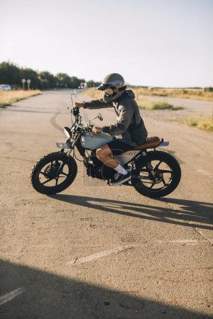 Téléchargez les photos : Biker sur une moto de course de café sur la route au coucher du soleil. - en image libre de droit