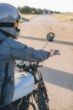 Téléchargez les photos : Biker sur une moto de course de café sur la route au coucher du soleil. Vue arrière. - en image libre de droit