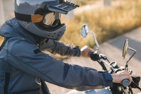 Foto de Un motociclista en un casco se sienta en una motocicleta en la carretera contra el atardecer. - Imagen libre de derechos