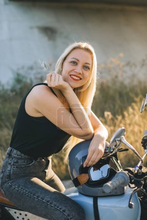 Foto de La chica motociclista se sienta en una motocicleta. Joven hermosa mujer rubia sentada en una motocicleta en la carretera al atardecer. - Imagen libre de derechos