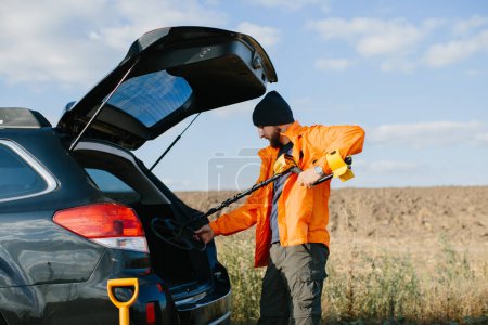 Téléchargez les photos : Un jeune homme sort un détecteur de métaux de la voiture. - en image libre de droit