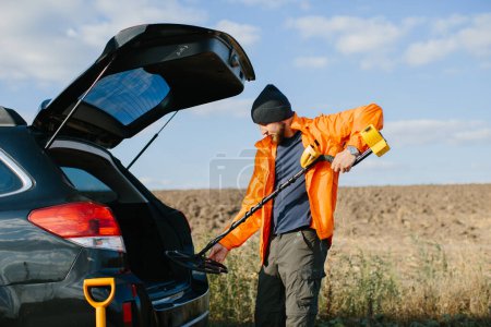 Photo for A young man takes out a metal detector from the car. - Royalty Free Image