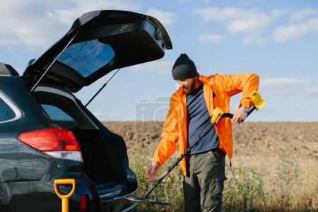 A young man takes out a metal detector from the car.