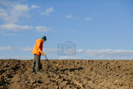 Photo for A man enjoys recreational archeology with a metal detector in a field - Royalty Free Image