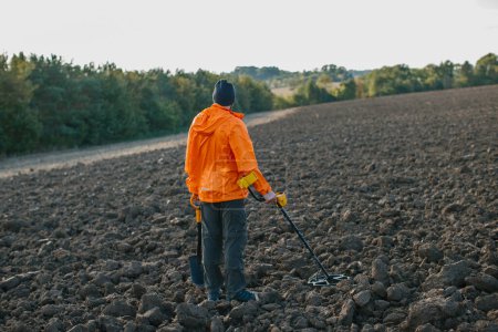 Photo for A young man searches for treasure with a metal detector in a plowed field. - Royalty Free Image